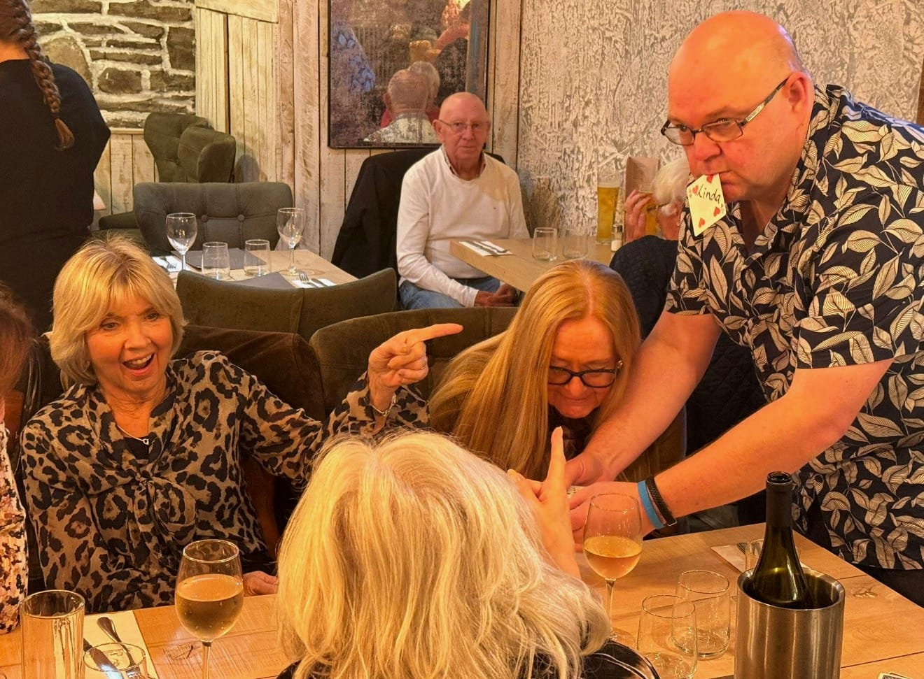 Jason performing a card trick at a restaurant table while a guest points and laughs