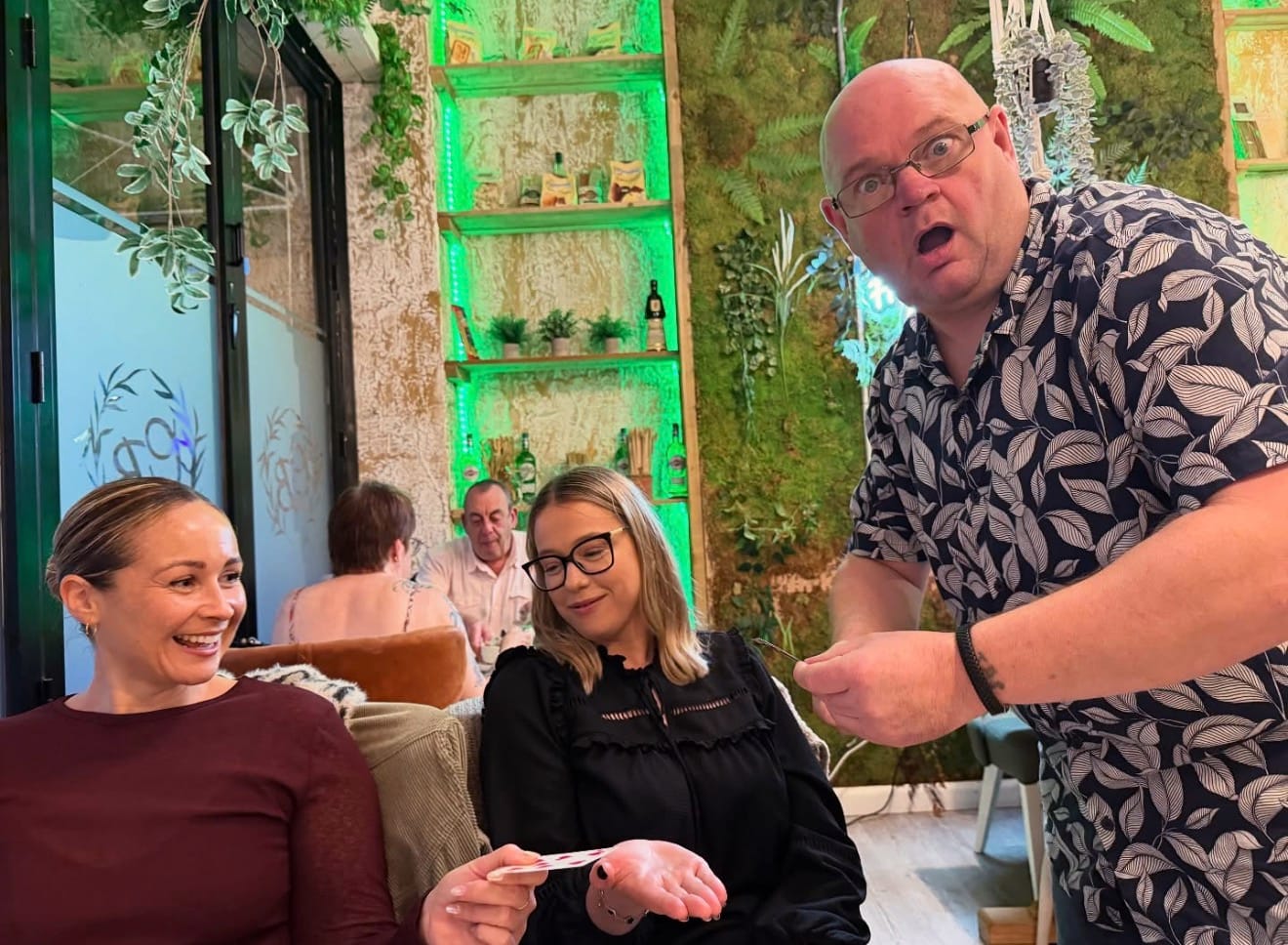 Jason looking astonished during a card trick as two seated guests smile at a playing card