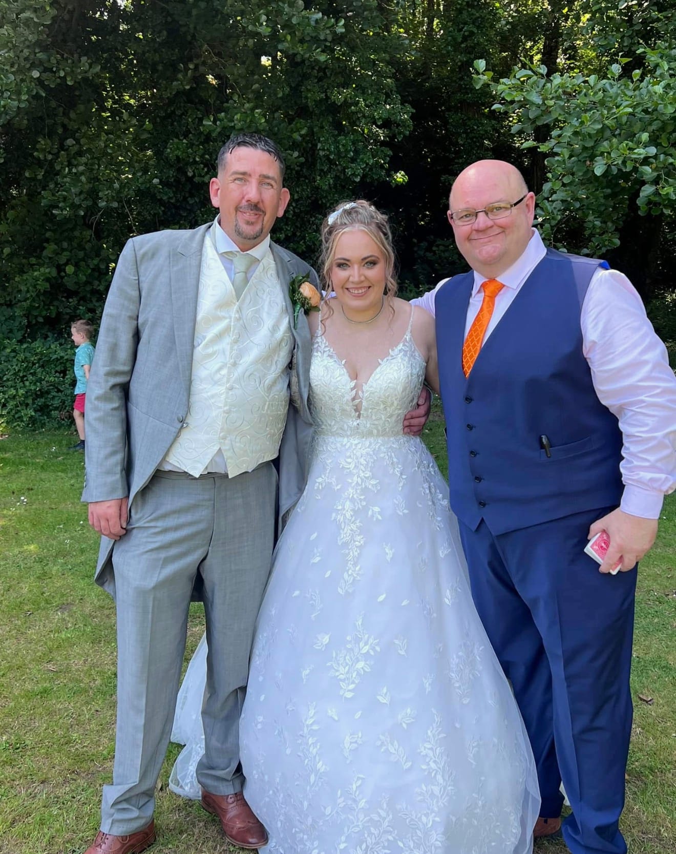 Jason with a bride and groom in a garden on their wedding day, holding a deck of cards